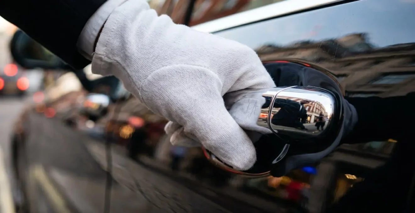 Close-up of chauffeur's gloved hand opening rear door of luxury vehicle, focusing on professional service details